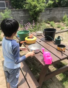 庭のピクニックテービルに水を入れた容器を並べる息子