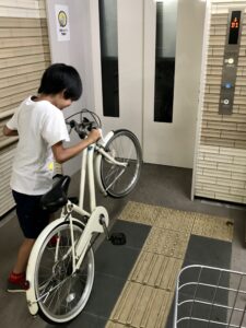 地下通路のエレベーター前で自転車の前輪を持ち上げる息子